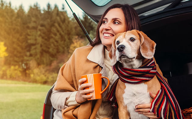 Woman sits on her car with her dog. 