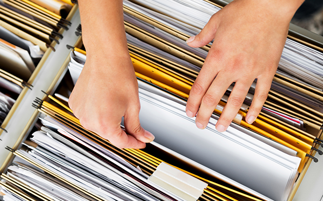 Two hands going through papers in a filing cabinet.