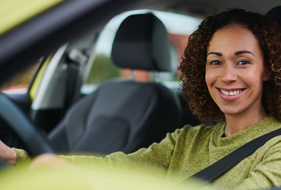 Woman sitting in her car looking at the camera smiling. 