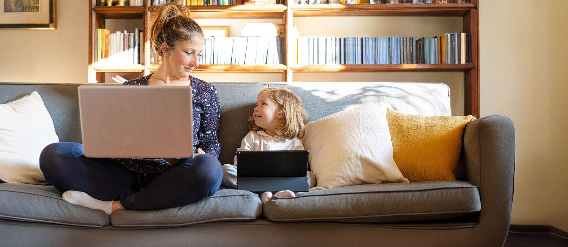 Mom and child looking at each other while they are on their electronic devices. 