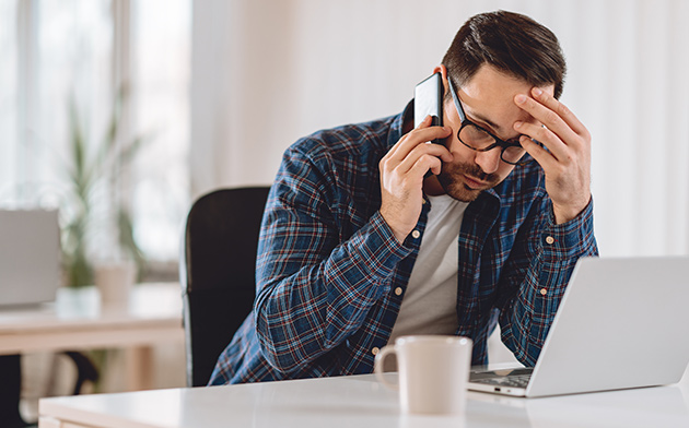 Frustrated man looking at laptop while on the phone.