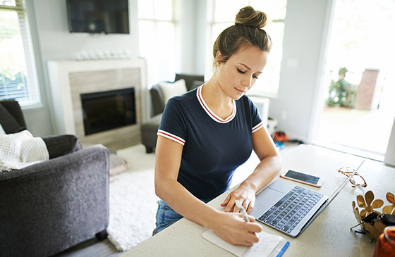 Girl writing on paper near a computer