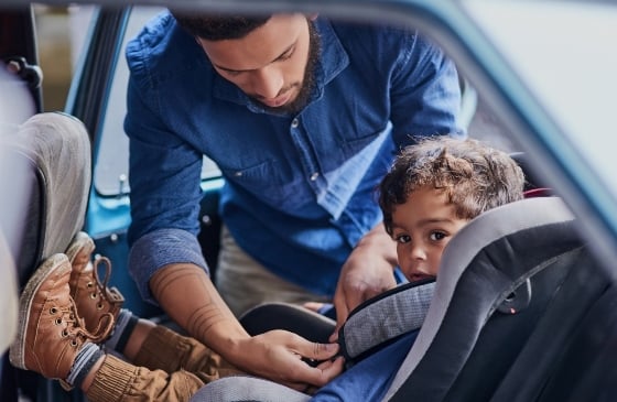 Father fastening son's car seat belt inside the car.