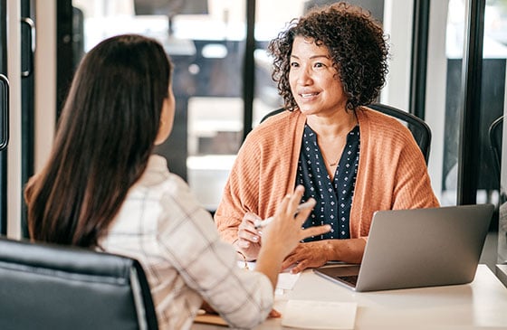 Two women sitting down talking about business. 