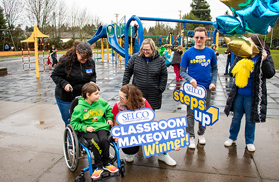 Image of a woman holding a SELCO classroom makeover winner sign. 