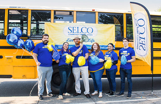 SELCO community credit union employees standing in front of a bus showing their appreciation for educators. 