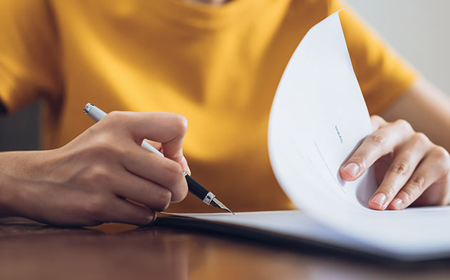 A person's hands at a desk writing on a stack of paper.