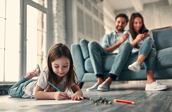 Young girl colors while parents sit on couch.