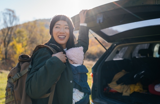 A mom carrying her baby and shutting the car trunk.