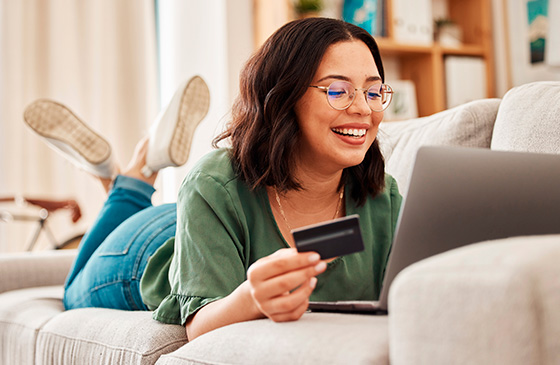 Woman laying on her bed looking at her credit card and laptop. 