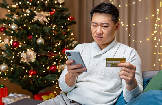 Man sitting on the couch with his phone and his credit card looking concerned. 