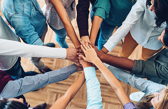 Group of people putting their hands together for a cheer.