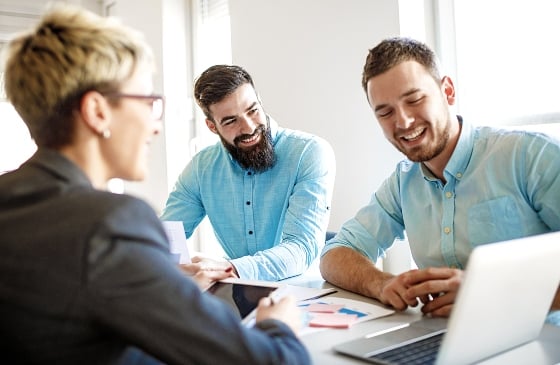 Two man with a business women looking at a laptop.