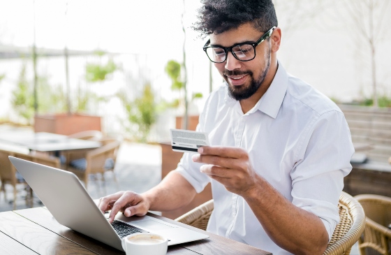 Men looking at a credit card while typing on his laptop.