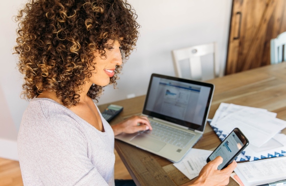 Woman looking at her phone with a laptop open on the desk.