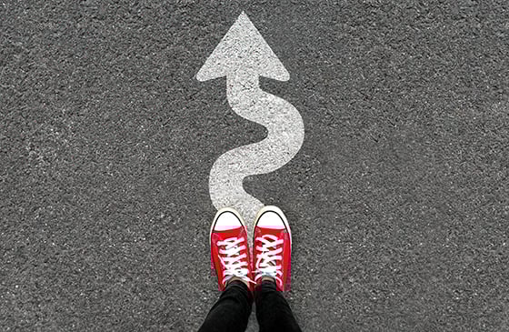 Person standing in red shoes in front of a winding arrow. 