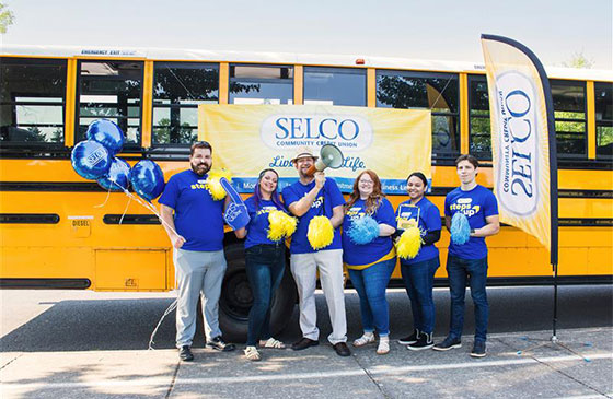 SELCO staff standing in front of a school bus holding signs. 