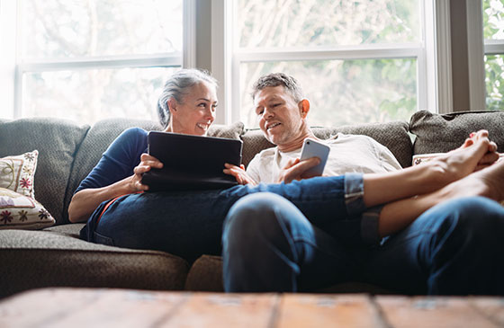 Older couple relaxing on couch looking at a laptop. 