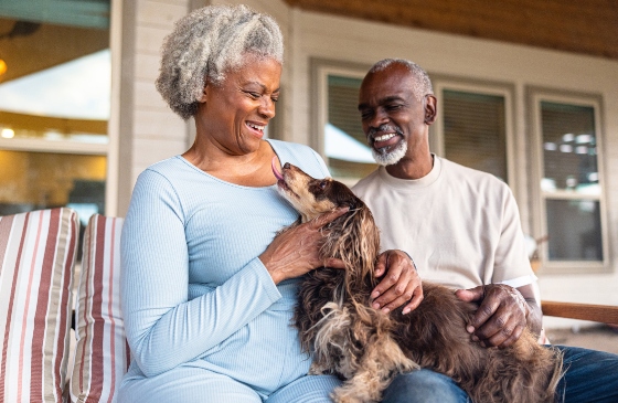 An older couple sitting on their porch, smiling with their dog. 