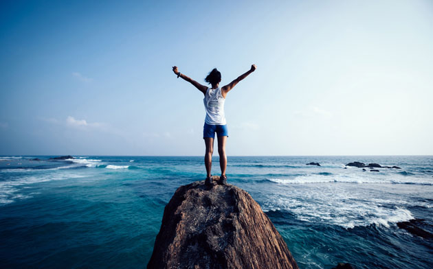 Person standing at the ocean with arms in the air