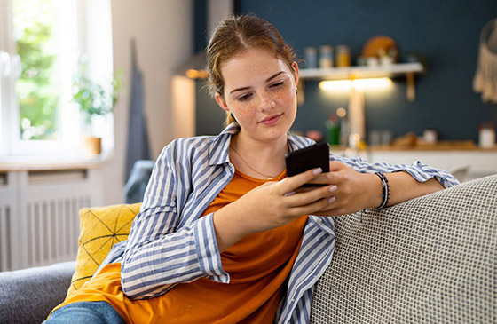 Woman sitting on her couch smiling looking at her phone.